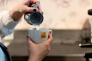 Manos de mujer vertiendo la crema de un capuchino en una taza oficial Filicori Zecchini.